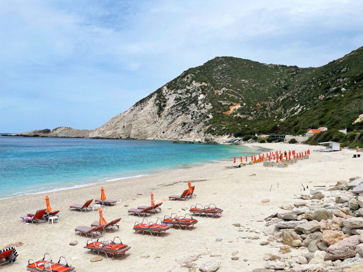 couples holiday to greece view of white sand beach blue water and lounge chairs along coast