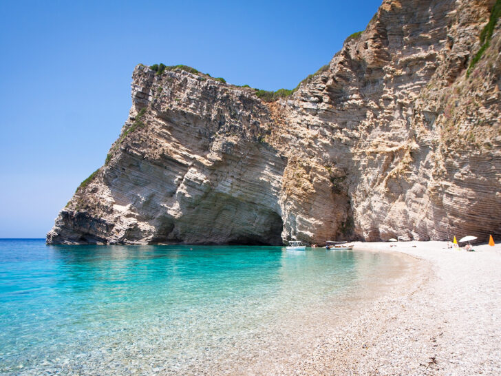 Paleokastritsa Bay Corfu best greek islands for couples view of beach and massive cliffside bright teal water on sunny day