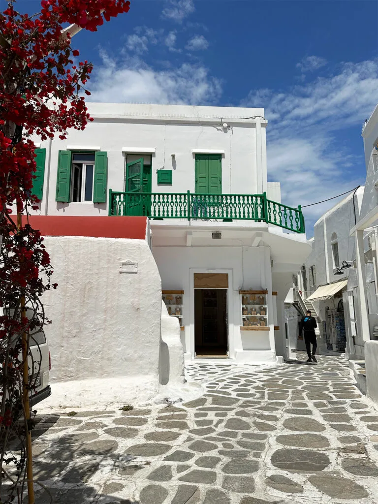 couples holiday to Greece view of white and stone streets with white building green accents and red flowers