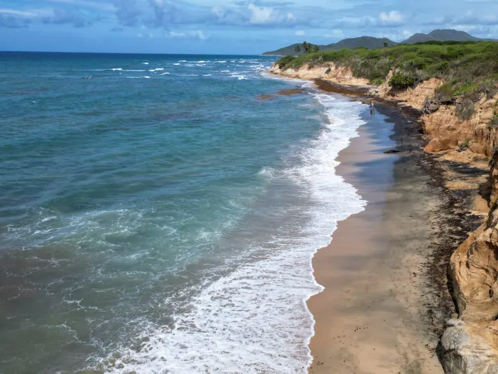 beach from above with hilly shoreline white wave blue water