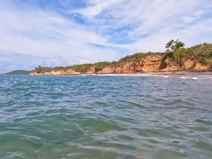 view of coastal shore from water with clouds in the sky