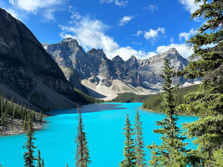 Banff alberta Canada view of bright teal water with trees and mountains in distance