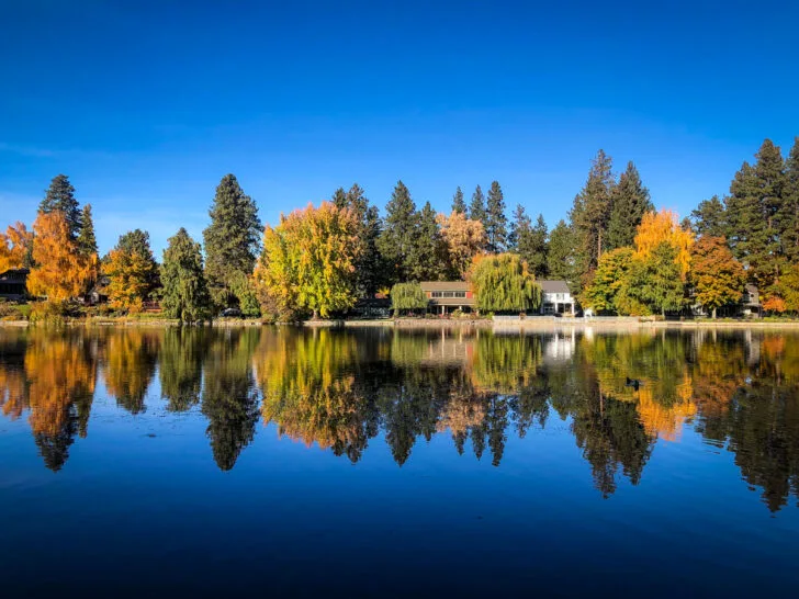 places to visit in October in usa view of blue lake water with cabin and bright trees and blue sky with reflection