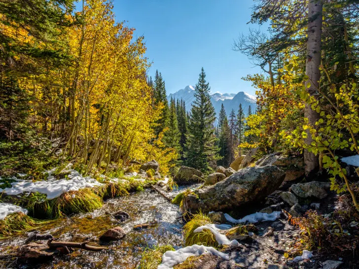 creek with snow yellow foliage on trees and mountains in distance