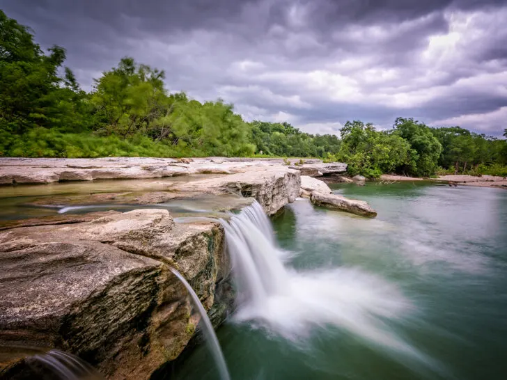 water falling over rock into pond on cloudy day