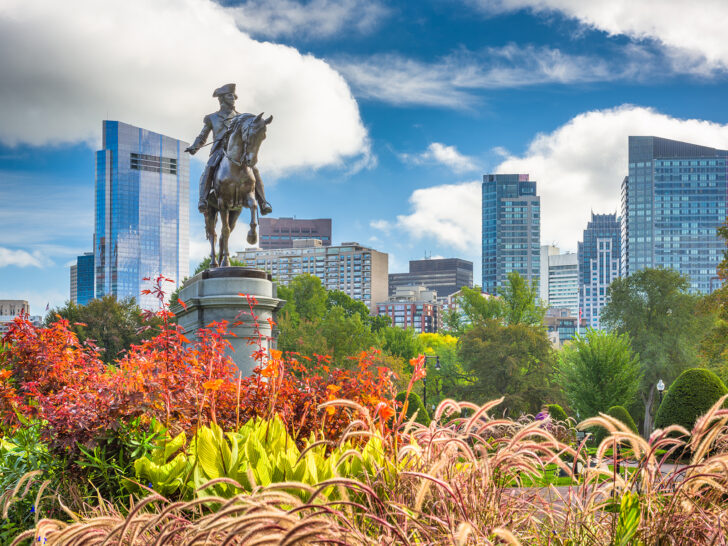 statue in fall foliage with city in distance in downtown Boston MA