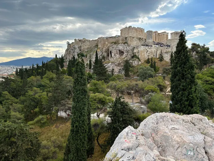 view of rocks and trees with acropolis in distance on 2 day athens itinerary