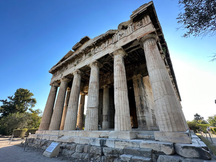 large building with 6 columns set up on stone with blue sky during athens itinerary
