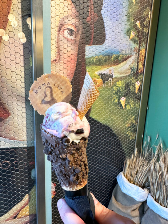 hand holding ice cream cone with Mona Lisa printed on cookie sticking out of ice cream and tile mosaic behind