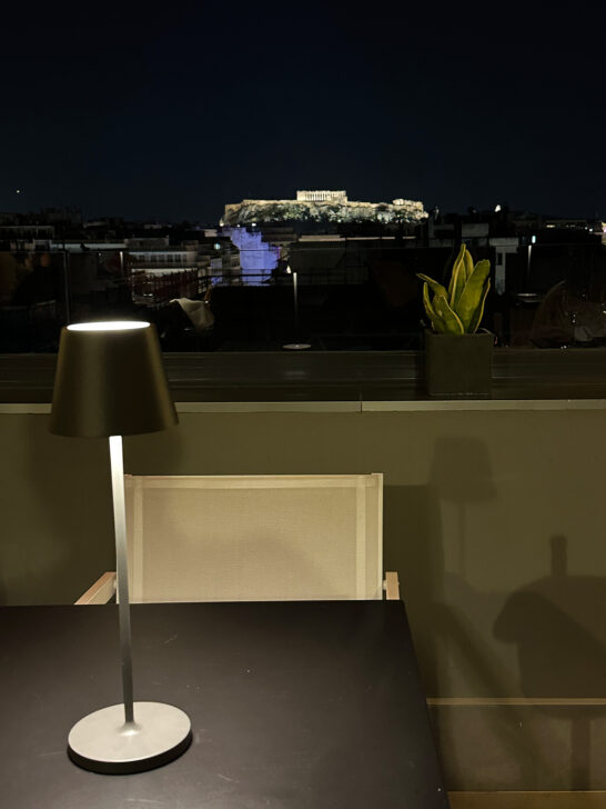 table at night on rooftop restaurant with parthenon in distance lit up