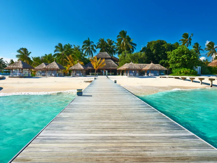 Maldives beach with beach huts and walkway over teal water best countries to visit in February 