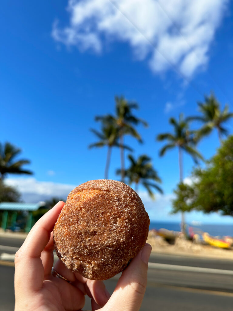 Kihei things to do view of hand holding malasada with palm trees in background