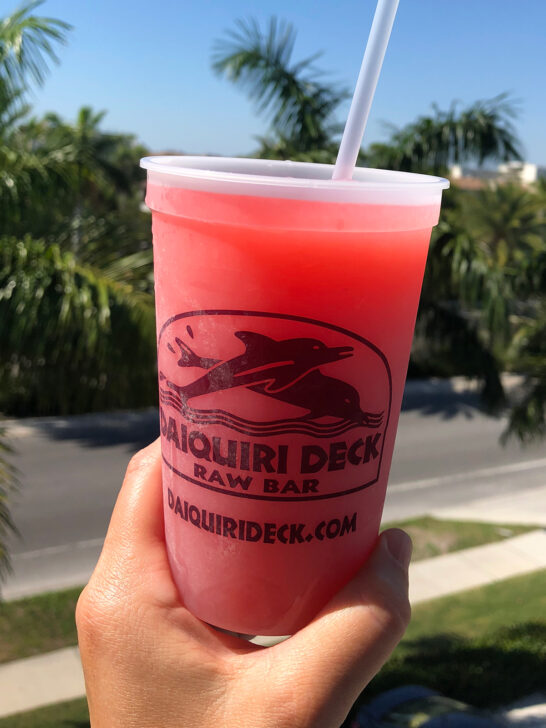 hand holding cup that reads daiquiri deck raw bar with pink frozen drink inside