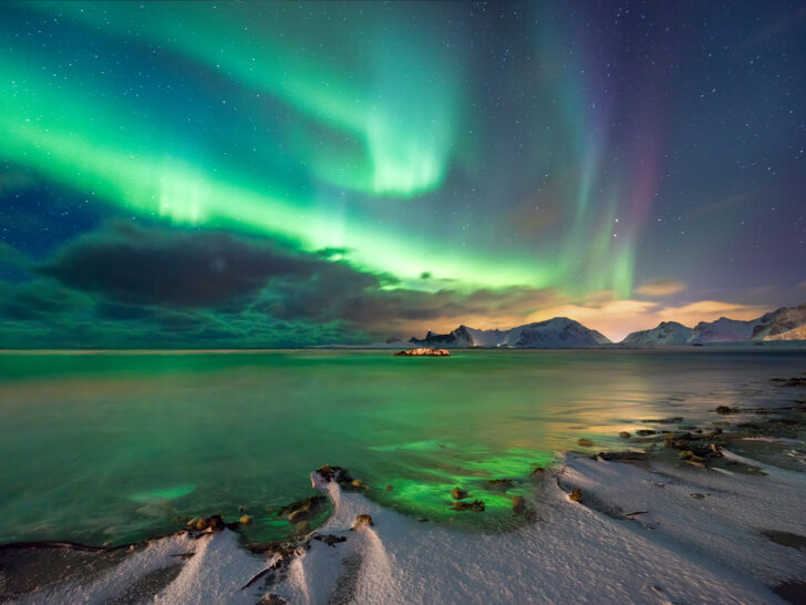 where to travel in February view of norway and northern lights green and purple spread across the sky