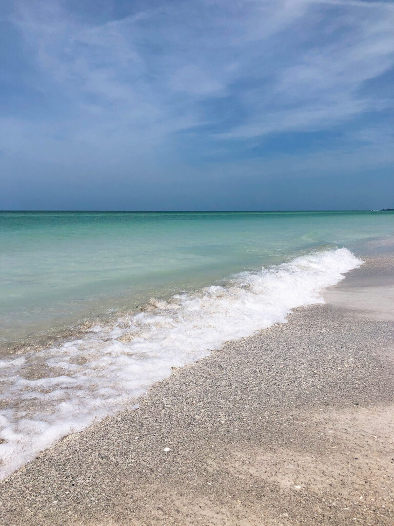 Anna Maria island beaches view of white wave on light colored sand with teal water blue sky