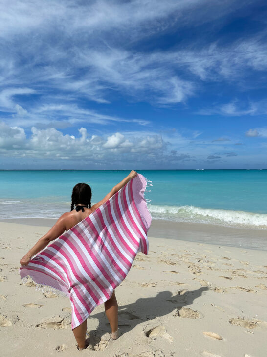woman holding white and pink towel with beach behind