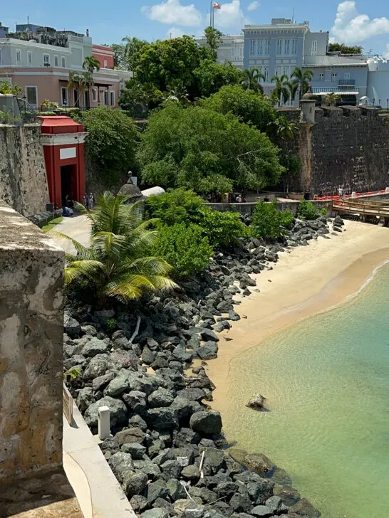 red door along large wall of city and black rocks small beach green water