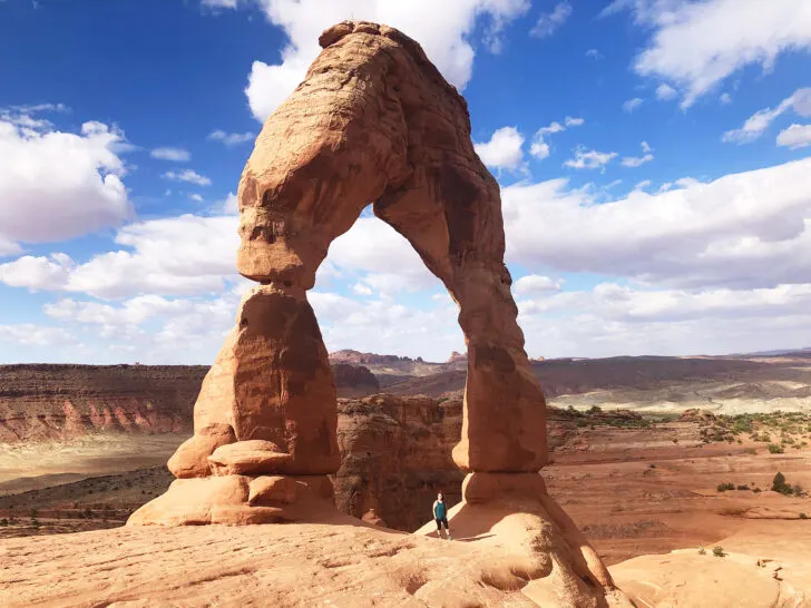 Moab Utah things to do with woman standing under Delicate Arch, Arches National Park