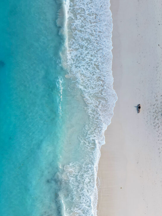 woman laying on the sand with blue water and white wave after Bahamas drone registration