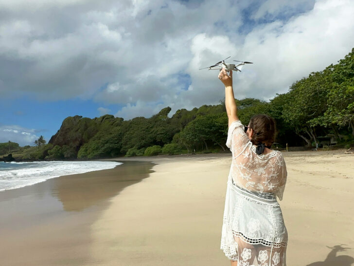 woman holding drone up above her head on beach after going through a drone pre flight checklist