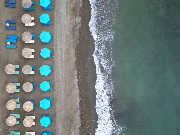 tan and blue beach umbrellas on dark sand beach with green water