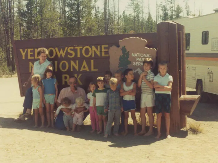 family trip to yellowstone national park with a bunch of kids and RV in front of the Yellowstone National Park sign