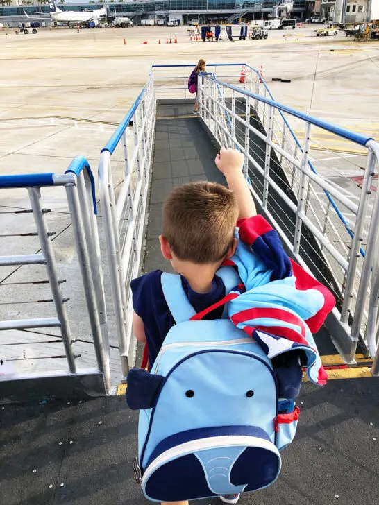 flying with kids and little boy with elephant backpack walking on outside jetway off plane