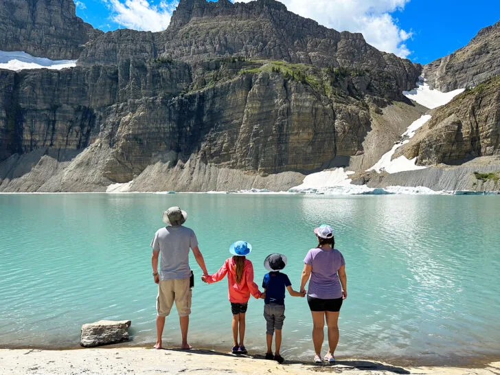 two parents and two kids standing at teal lake with mountain in distance