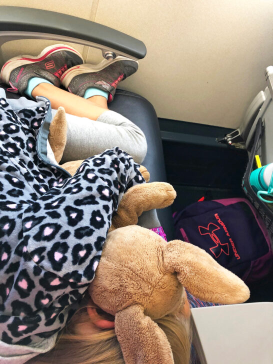 little girl laying down on airplane seat flying with kids