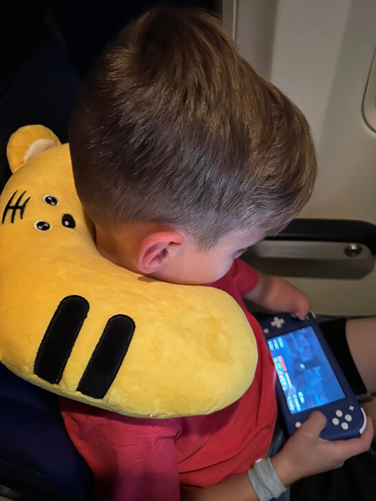 boy with neck pillow playing handheld game air travel with kids