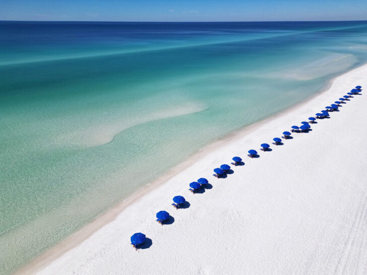 30a Florida beaches view of blue and teal water with blue beach umbrellas lining the waters edge