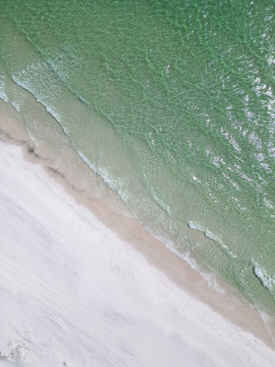 emerald colored water waves crashing into white sand from above