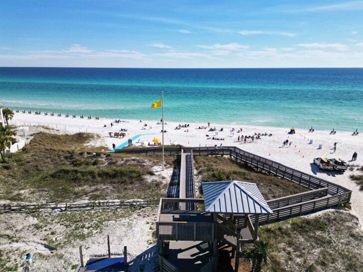 boardwalk with tower and yellow beach flag with people on white sand beach blue water on the best 30a beaches