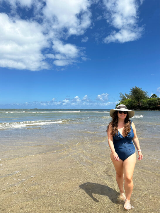 mid-size woman walking in water in blue bathing suit and sun hat with blue sky and ocean