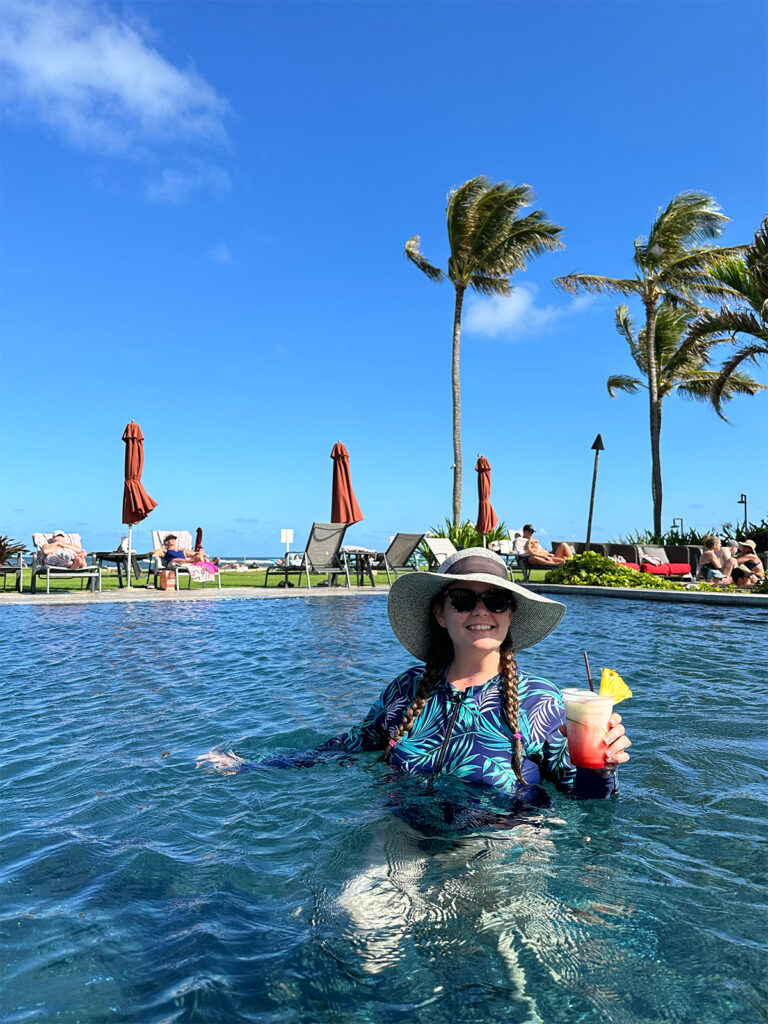 woman in pool with long sleeve swimming suit and palm trees in distance
