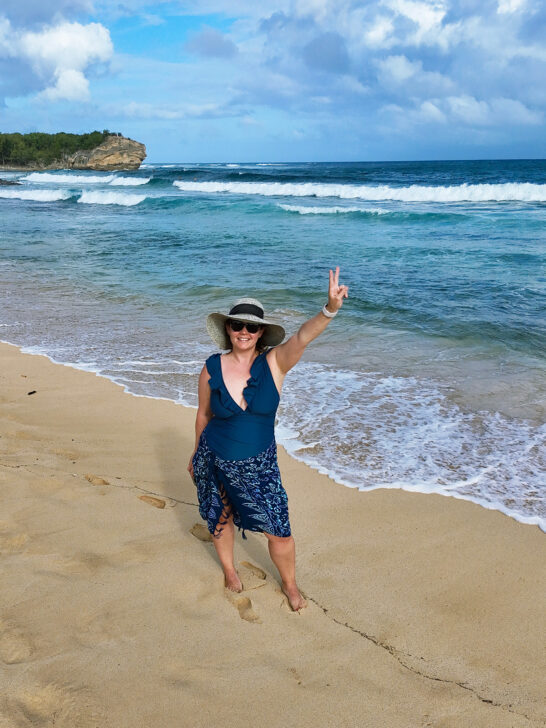 woman wearing blue suit and sarong with beach hat and blue water behind