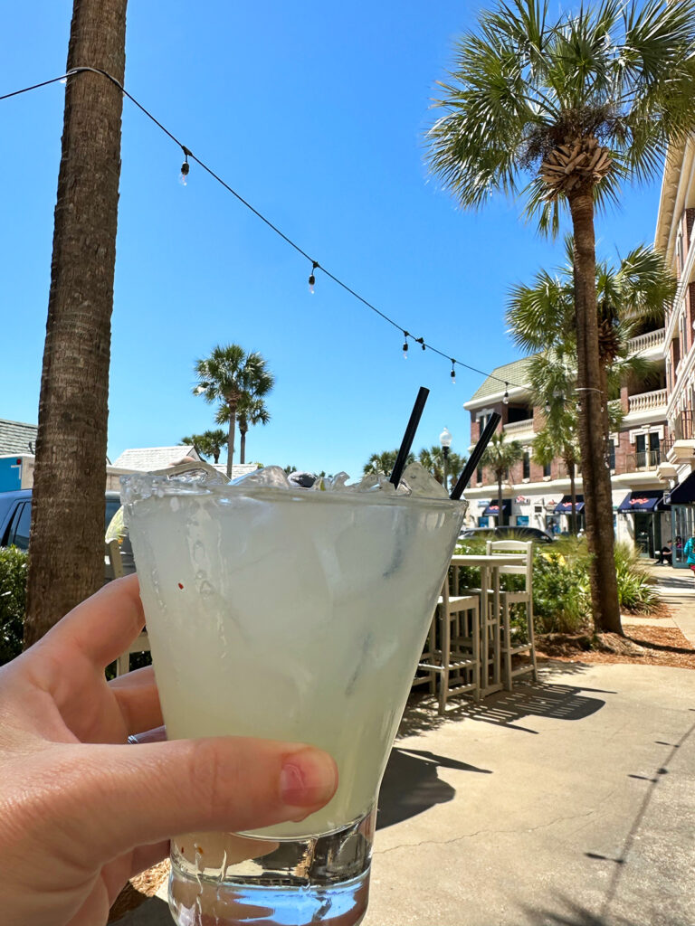 hand holding lime margarita with palm trees