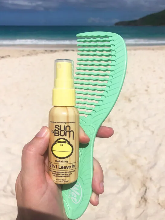 hand holding comb and sun bum conditioner with beach in distance