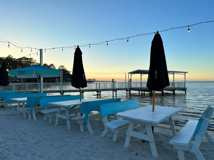 sunsetting in distance with restaurant shorefront with picnic tables and umberellas 30A florida