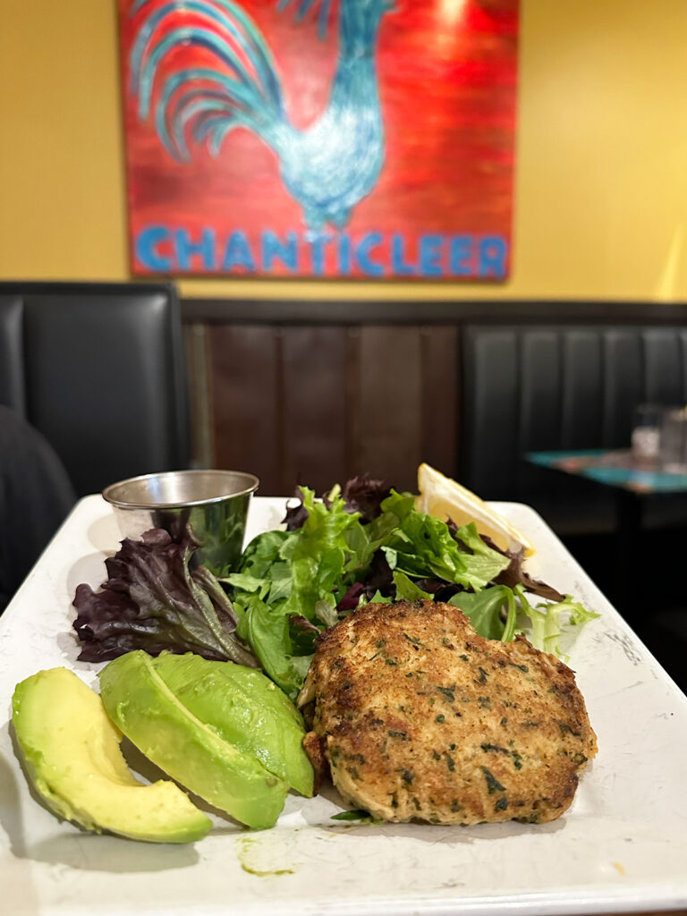 crab cakes with lettuce and avocado with painting in distance that reads chanticleer best restaurants 30a Florida