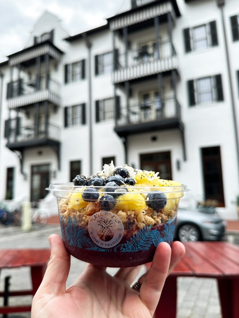 acai bowl with blueberry and pineapple with black and white building in distance in rosemary beach FL