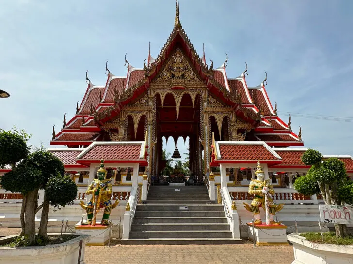 large temple with red gold and white with large statues in front and steps up during a Bangkok 2 days vacation