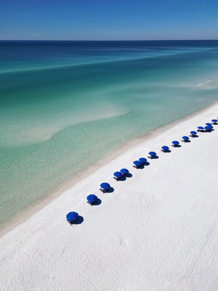 crisp white sand with ocean varying shades of blue and blue beach umbrellas photo taken with drone how to fly a drone