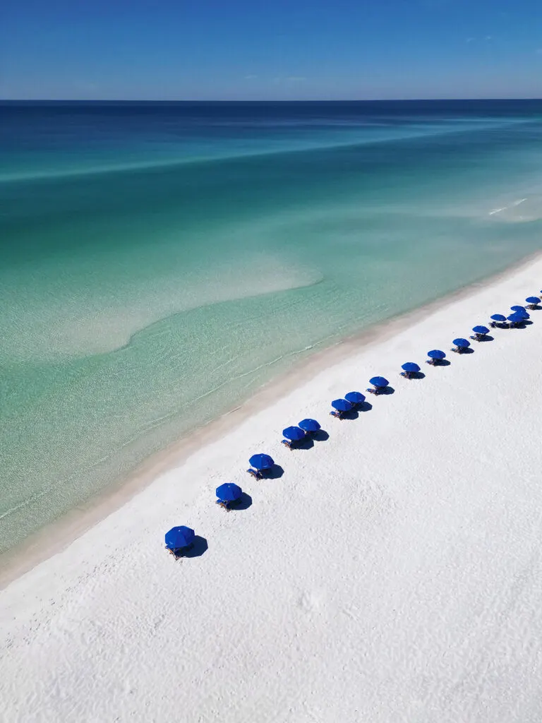 crisp white sand with ocean varying shades of blue and blue beach umbrellas photo taken with drone how to fly a drone