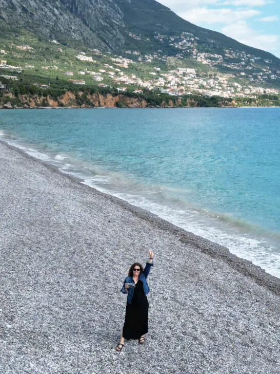 woman standing on rocky beach with mountain in distance flying a drone