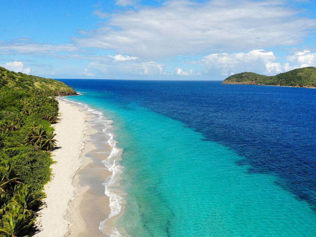 learn how to take drone photos view of teal and blue water along white sand beach with green coastline