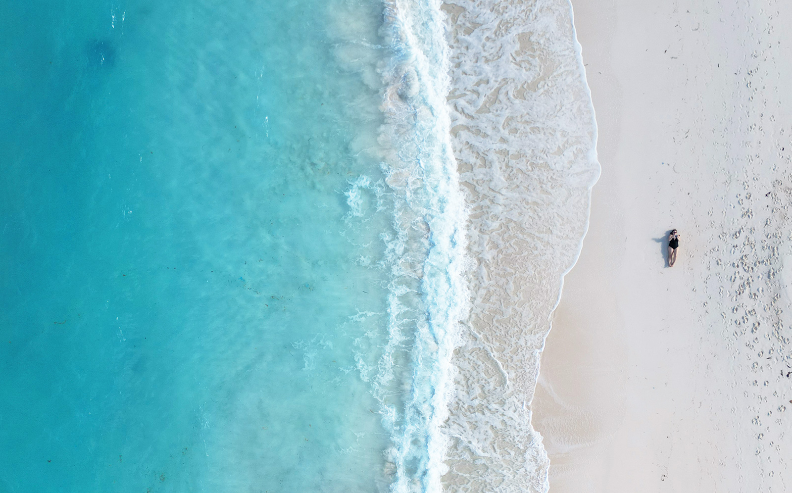 Bahamas travel guides aerial view of beach with blue water white wave with woman laying on sand via drone photo