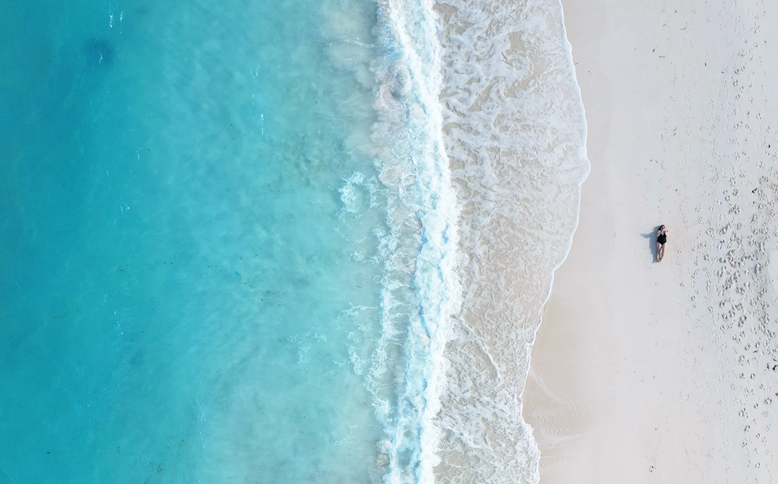 Bahamas travel guides aerial view of beach with blue water white wave with woman laying on sand via drone photo