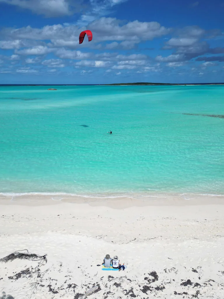 person kiteboarding over water with couple sitting on beach in the bahamas