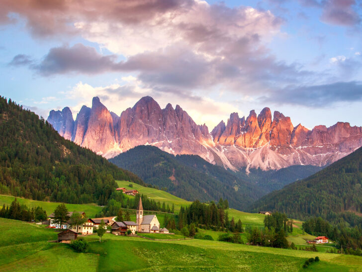 travel bucket list view of Dolomites, Italy with view of church on grassy meadow and mountains in distance